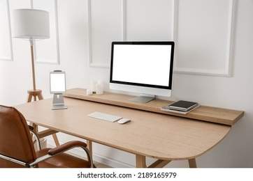 Modern workplace with computer and tablet near light wall