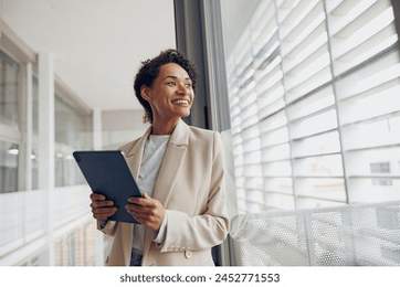 Pretty female manager with digital tablet standing on modern office background and looks away